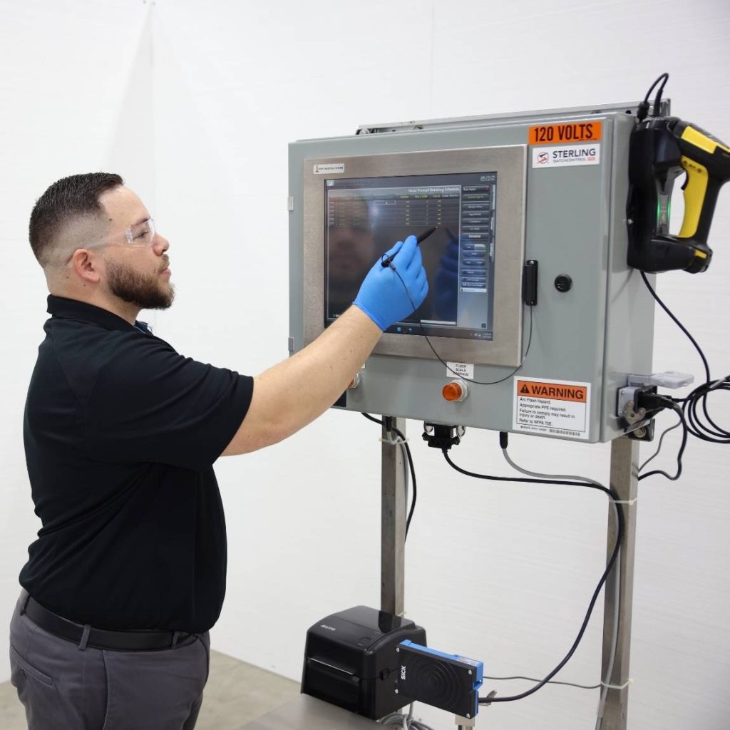 BatchControl Pro 2 | Sterling Systems & Controls Operator in safety glasses and blue gloves uses a touchscreen control panel on an industrial machine labeled 120 volts.