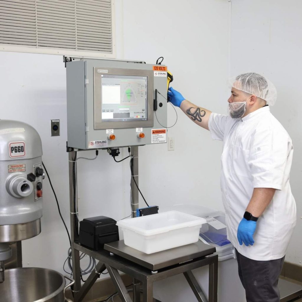 BatchControl Pro 3 | Sterling Systems & Controls Lab technician wearing a hairnet and blue gloves operates a touchscreen control panel on industrial equipment in a cleanroom setting